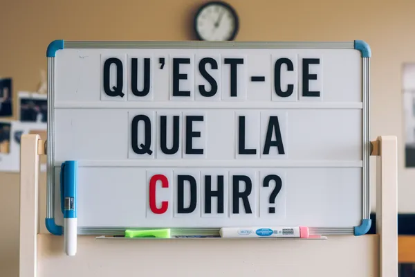 Tableau blanc à lettres amovibles affichant la question Qu’est-ce que la CDHR ?, sous une horloge murale.