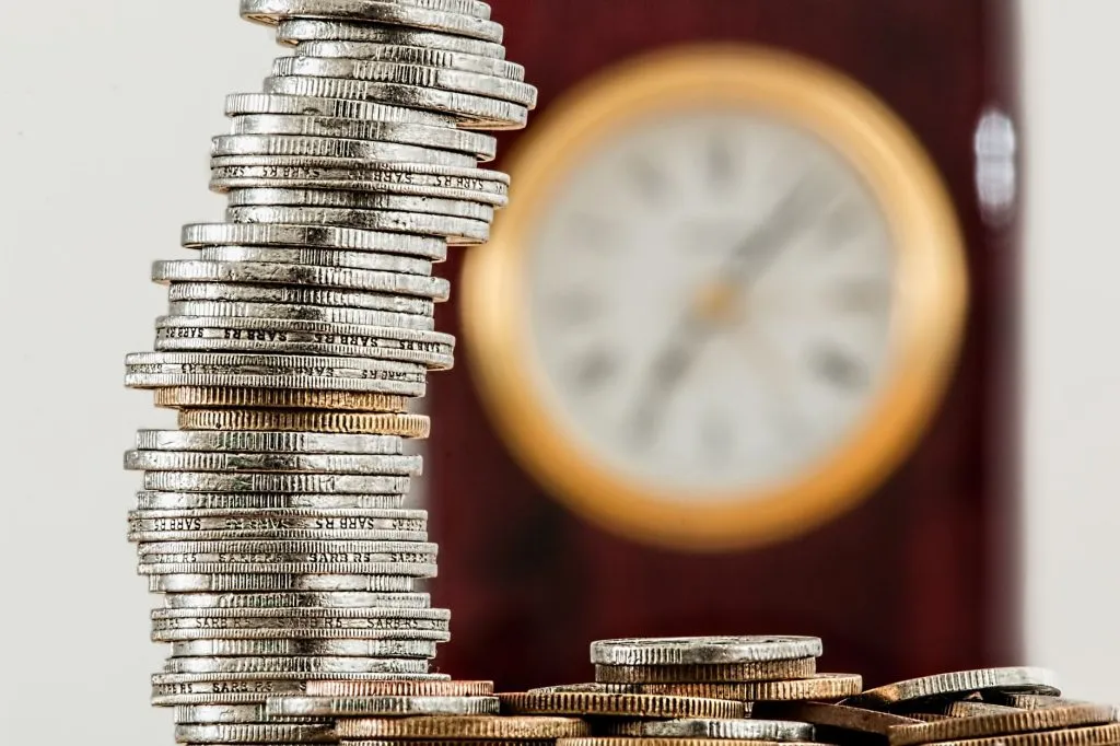 Pièces de monnaie empilées avec horloge floue symbole temps et argent