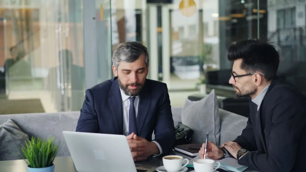 Deux consultants en costume échangeant autour d'un ordinateur portable dans un café