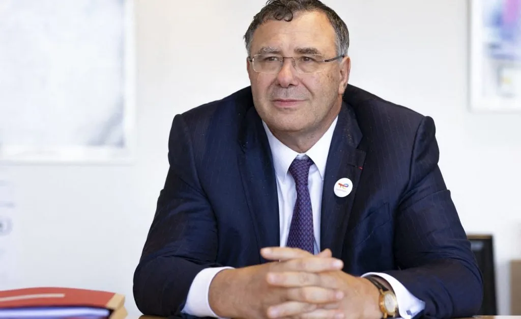 Patrick Pouyanné, en costume sombre et cravate, assis à une table de réunion, mains jointes