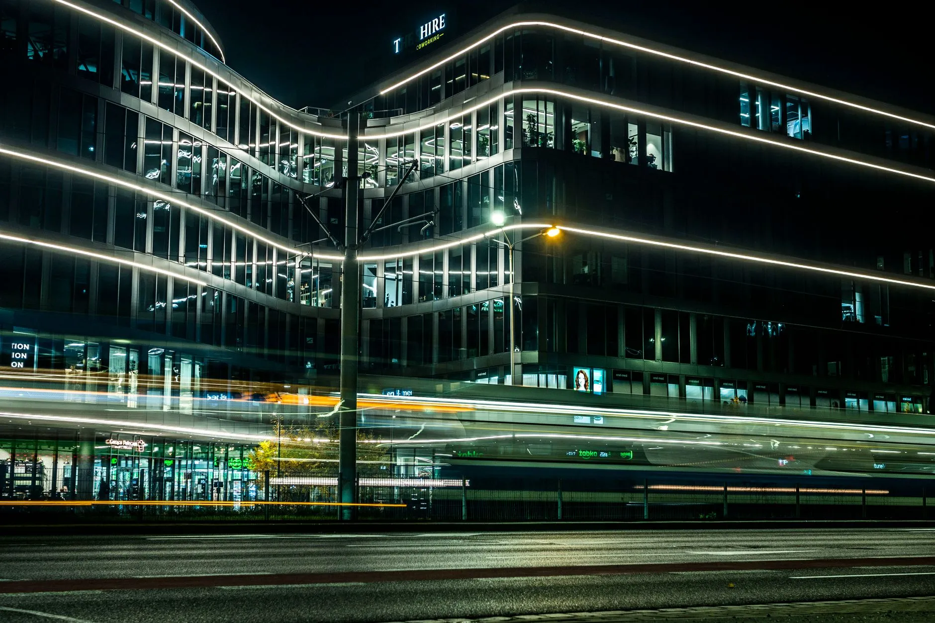 Immeuble de bureaux vitré éclairé de nuit, traînées lumineuses de la circulation au premier plan